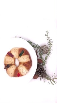 Traditional Rosca de Reyes bread in Mexico on white plate on white background turning alongside the walnut and fresh rosemary decorations lock dawn camera  top view