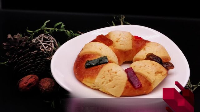 Mexican Three Kings bread with candied fruit, on black background turning alongside the walnut and fresh rosemary decorations lock dawn camera