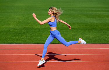 Fototapeta premium Woman in sportswear jogging on stadium. Sportswoman in sportswear jumping. Woman running jump on stadium track. Fitness woman on stadium, run. Young fitness woman runner running on stadium track
