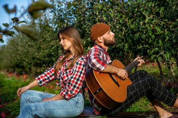 Couple singing together on a picnic in park. Young pretty couple having fun outdoors guitar while sitting at the campsite. Outdoor holiday lifestyle concept. Man playing guitar for his girlfriend