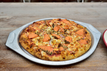 A freshly baked pizza topped with salmon, onions, and herbs on a metal tray