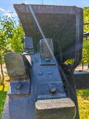 A black and grey object with a shiny surface. The shiny surface is reflecting sunlight. The object is surrounded by trees