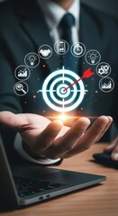 Businessman holding holographic target with arrow in bullseye, surrounded by business icons, representing strategy, goals, and success.