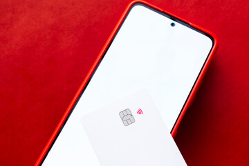 Smartphone and a credit card on a vibrant red surface, emphasizing modern and secure financial transactions.