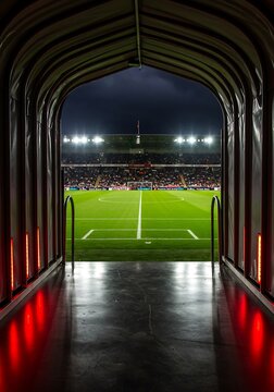 The powerful contrast of a dark, red-lit tunnel leading to the brilliant spectacle of a crowded football stadium at night