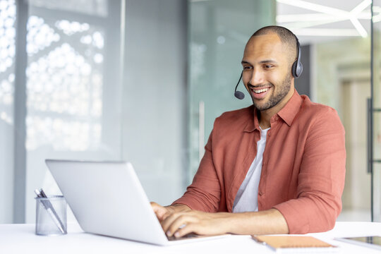 A professional individual using a laptop and headset for a video call in a bright modern office, emphasizing communication and productivity.