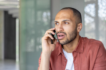 A young man appears concerned while having a phone conversation in a modern space. The image captures emotion and communication in a professional yet casual setting.