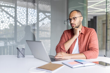 A thoughtful individual working on a laptop, epitomizing concentration in a modern office setting.