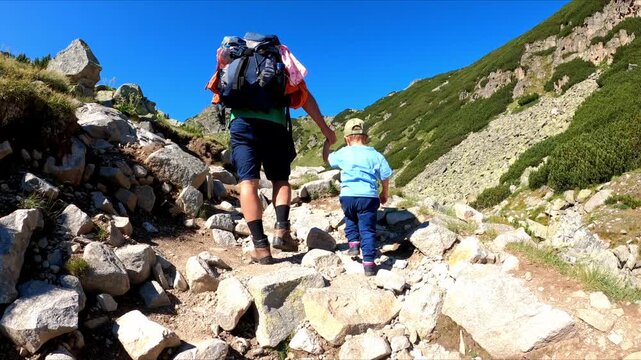 Father and child hike up a rocky mountain trail on a sunny day. Hiking and family idea. Adventure and outdoor concept.