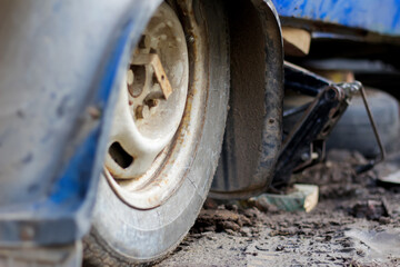 close-up of an old car's wheel and a jack. The image, with a vintage aesthetic, highlights the details of the blue car
