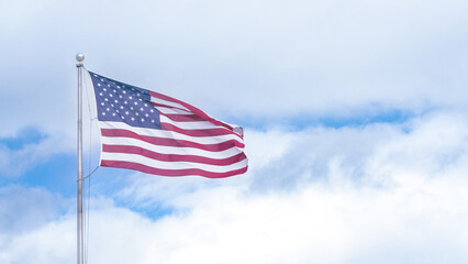 American flag waving gracefully against a backdrop of blue sky and soft white clouds, symbolizing patriotism and national pride