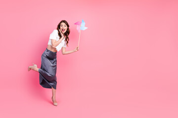 Elegant young woman holding a pinwheel on a pink background, radiating happiness and charm in a fashionable outfit