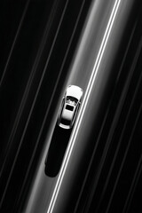 Silver car speeding along the asphalt highway, captured from above, evoking speed and motion in monochrome.