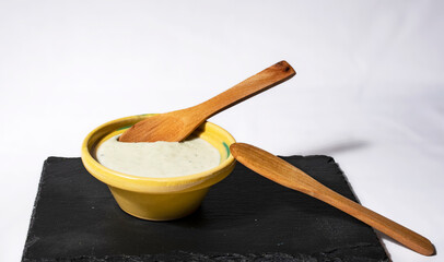 bol de salsa roquefort encima de un plato de pizarra negro con una cuchara de madera y fondo blanco