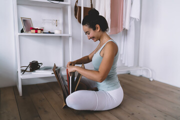 Smiling young woman arranging summer hat and clothes, enjoying light morning routine in minimal modern bedroom filled with calm and clarity.