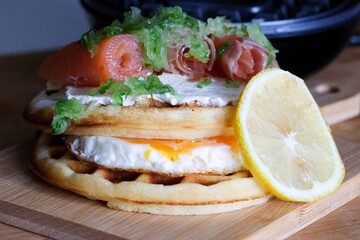 Close-up of waffles topped with creamy cheese and smoked salmon, drizzled with sauce. This is a delicious gourmet breakfast or brunch dish with rich flavors.