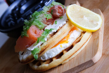 Close-up of waffles topped with creamy cheese and smoked salmon, drizzled with sauce. This is a delicious gourmet breakfast or brunch dish with rich flavors.