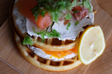 Close-up of waffles topped with creamy cheese and smoked salmon, drizzled with sauce. This is a delicious gourmet breakfast or brunch dish with rich flavors.