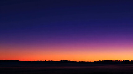 Fototapeta premium Deep indigo sky fades into vibrant orange horizon over silhouetted treeline sunset twilight