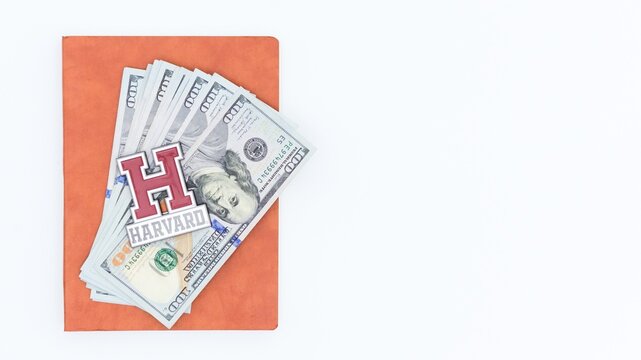 Education Funding Concept Stack of Money, Notebook, and Harvard University logo on White Background, Copy Space