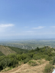 Naklejka premium Panoramic view of a green valley and hillside with a distant town under a clear blue sky