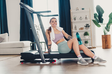 Fototapeta premium Sportsperson smiling after workout, sitting on a treadmill at home, showing active lifestyle and fitness dedication