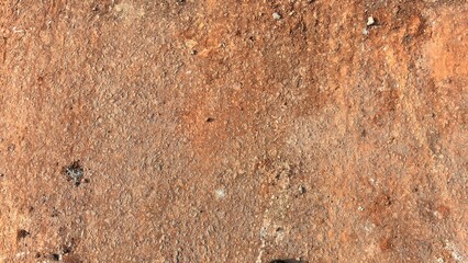 Rough reddish-brown dry earth texture with small stones and pebbles natural ground background.