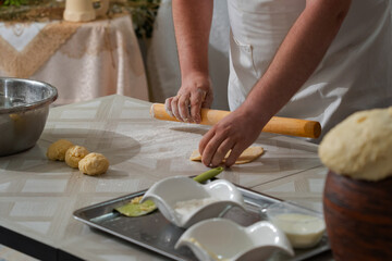 A male cook prepares dough for pies, his hands are stained with wheat flour