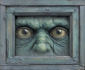 A close-up artwork of a creepy face with intense eyes within a wooden frame.