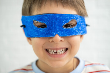 Cheerful strong little boy is wearing blue handmade mask like superhero playing at home.