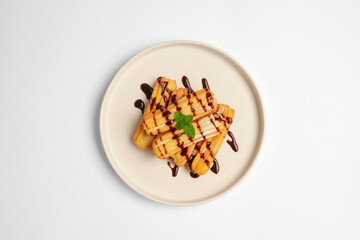 Top View of Delicious stack of golden churros drizzled with chocolate sauce and garnished with mint leaves, served on a white plate over a clean white background.