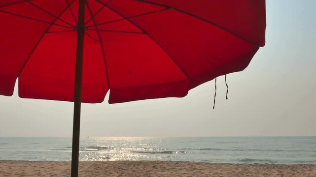Red beach umbrella on a sandy beach with ocean view on a sunny day