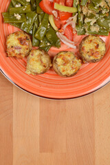 An orange plate holds a meal consisting of stuffed mushrooms, a cooked green bean and garlic salad, a fresh green bean and tomato salad, and green beans with breadcrumbs and cream with ample copy spac
