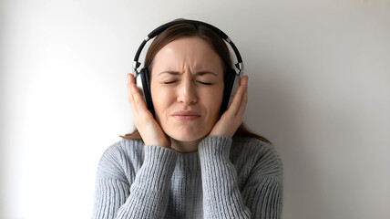 Autistic adult woman with noise cancelling headphones on light background showing discomfort from sensory overload autism ADHD hypersensitivity meltdown anxiety