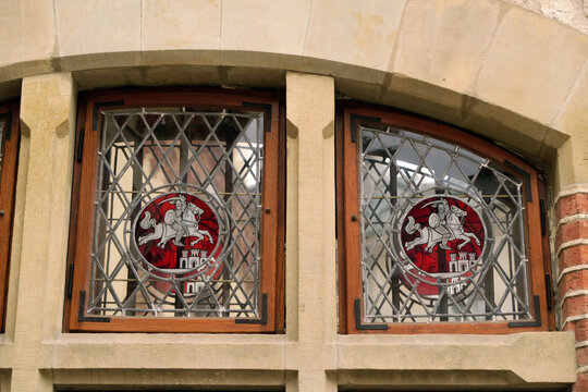 Kraków, Poland. A section of a historic stone building featuring three arched windows with decorative stained glass depicting a knight on horseback.