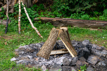 Stone fire pit with stacked logs, prepared for lighting a campfire on a grassy area.