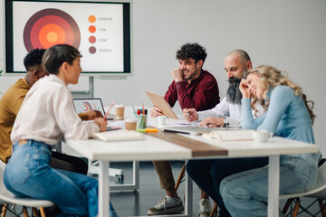 Marketing professionals laughing during business meeting in modern office