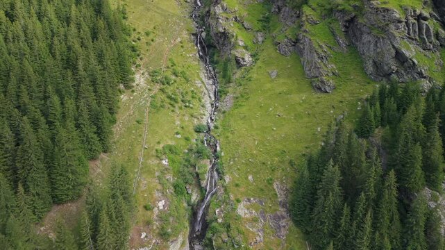 Aerial view of the road and landscape of the Transfagarasan Road in Romania with waterfall. The drone's camera rises into the air.
