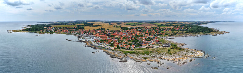 Aerial panoramic view of Svaneke on Bornholm Island Denmark surrounded by the Baltic Sea with red rooftops rocky coastline and lush countryside under a cloudy summer sky