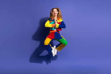 Cheerful Young Woman in Colorful Trendy Outfit Jumping Against Violet Background Expressing Happiness and Style