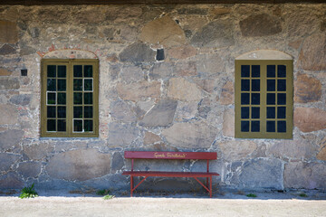 Rustic Stone Wall with Two Symmetrical Windows and a Red Wooden Bench Marked &ldquo;Gamle Fredrikstad&rdquo; in Historic Old Town Norway