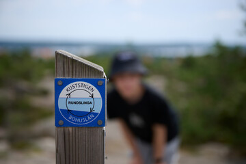Kuststigen Trail Marker in Focus with Hiker in Background on Rocky Coastal Path Near Str&ouml;mstad, Sweden