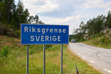 Blue Road Sign Marking Sweden National Border from Norway along Winding Rural Road