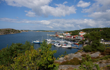 Scenic coastal harbor with boats docked at marina near colorful seaside village under partly cloudy sky on the island of Res&ouml; in Bohusl&auml;n, West Sweden
