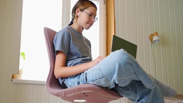 Teen girl school student wear headphones watching online webinar, talking through webcam looking at laptop. Teenager conducting video conference on computer at home, chatting online with friends. 4K