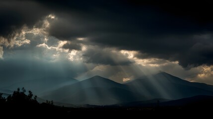 Sunbeams piercing through dark clouds over a mountain range.