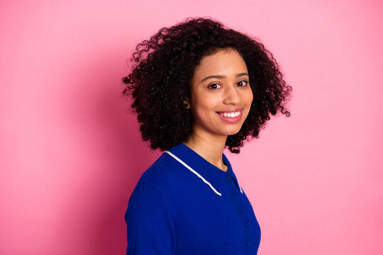 Attractive young woman with curly hair wearing blue polo shirt smiling against pink background