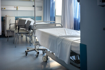 Interior of a vacant hospital room, featuring two adjustable beds, chairs, and medical equipment. A...