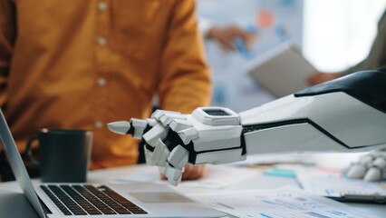 A futuristic robotic arm interacts with a laptop in a modern workspace, showcasing the blend of technology and human collaboration in today's innovative environments.Noogenesis
