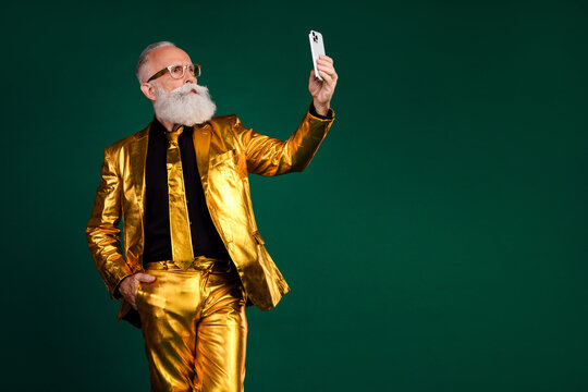 Elderly gentleman in glamorous golden suit taking a selfie on green background, embracing festive vibes of New Year's.